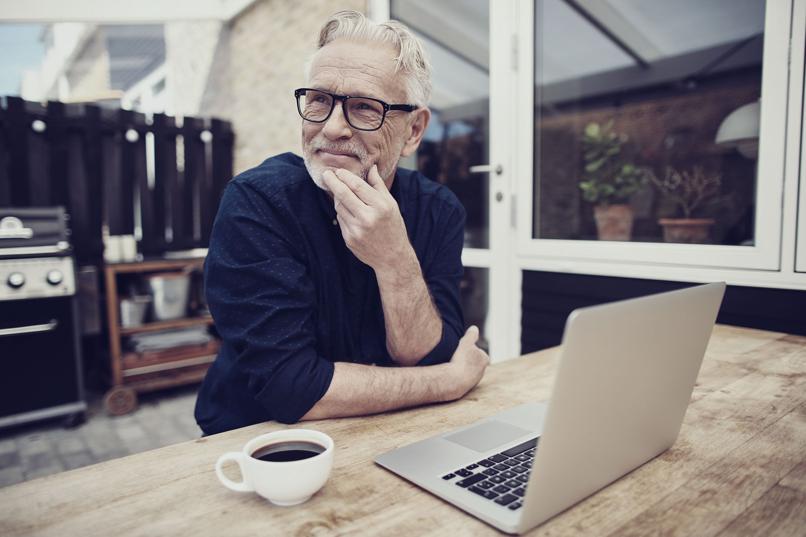 senior-man-sitting-outside-drinking-coffee-and-using-a-laptop