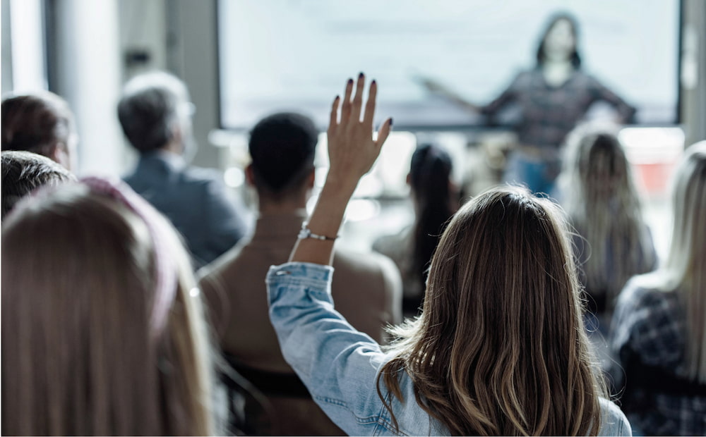 A woman raising in a classroom raising her hands in response to a presentation.