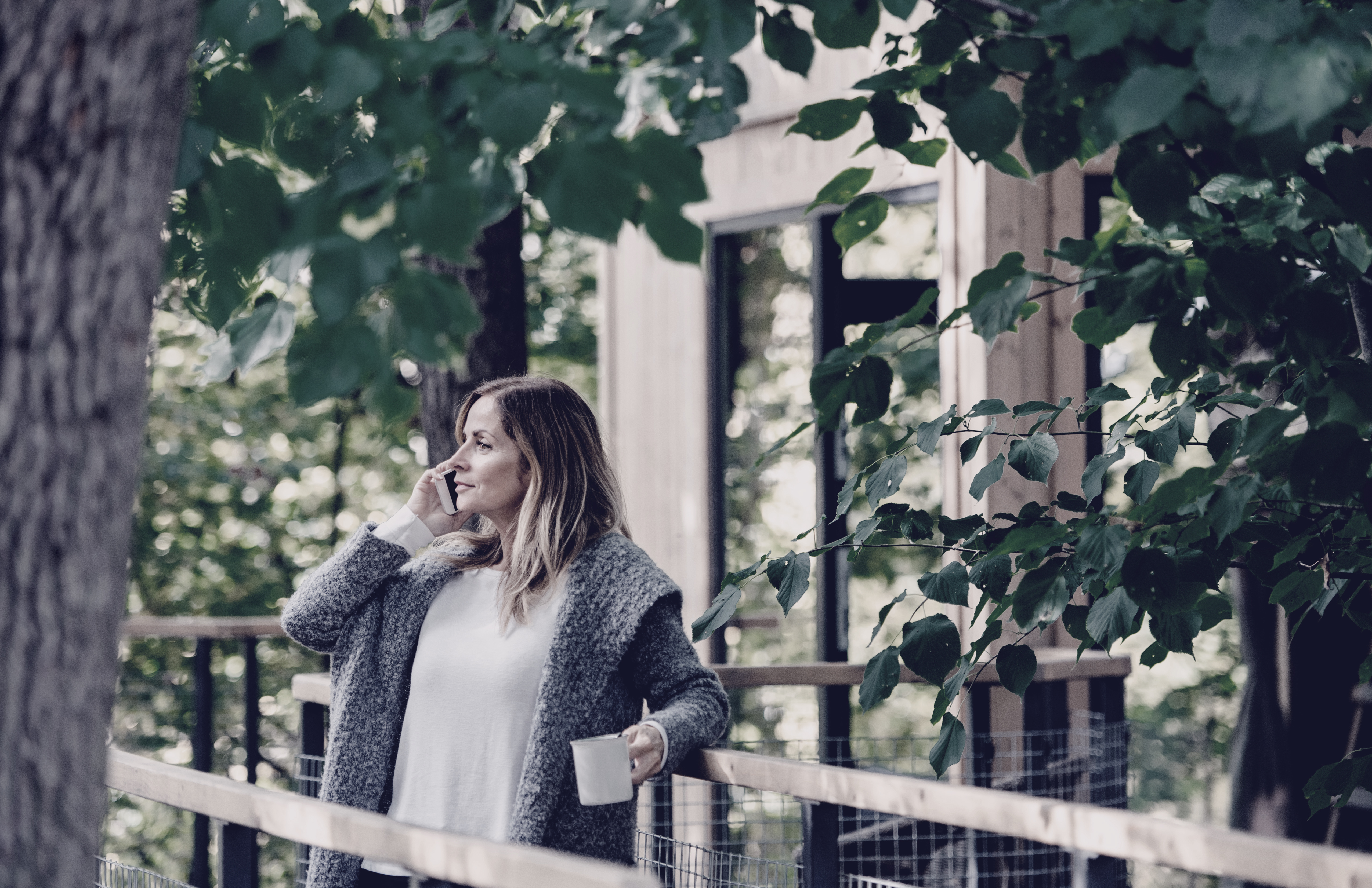 Mature woman with smartphone outdoors in front of a tree house
