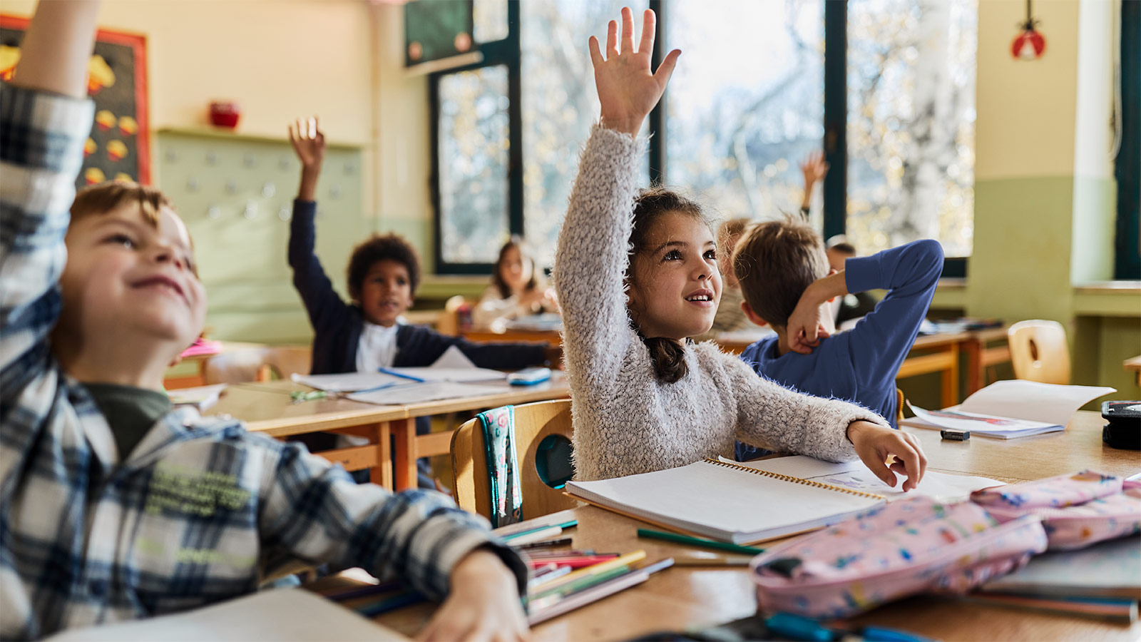 Glade folkeskoleelever, der rækker hånden op i en time i skolen.
