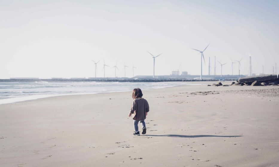 Child walking in the beach close to wind farm