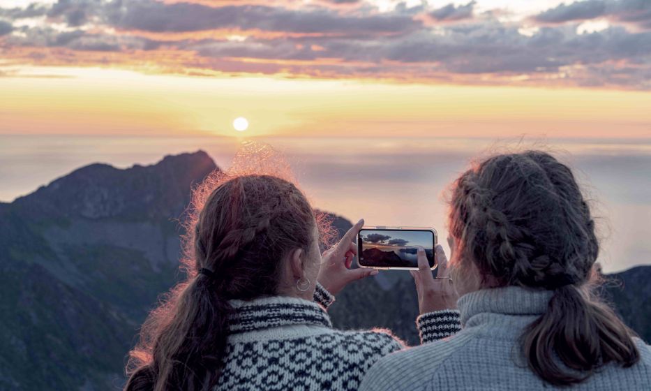 Women photographing sunset with smartphone