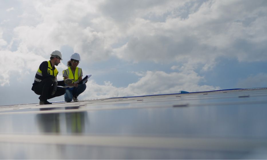 Professionals in safety vests examining a rooftop solar panel.