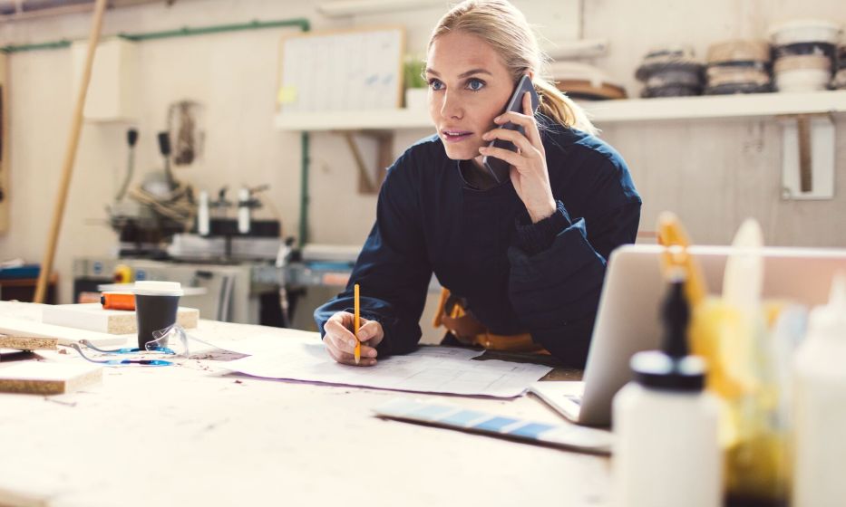 Kvinde står foroverbøjet over et bord og taler i mobiltelefon