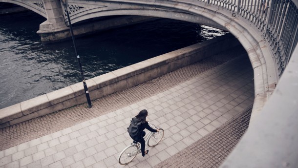 high-angle-view-of-businesswoman-riding-bicycle-on-footpath-by-canal-in-city