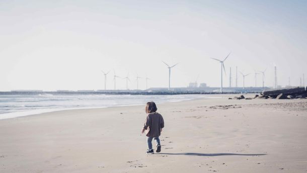 Child walking in the beach close to wind farm