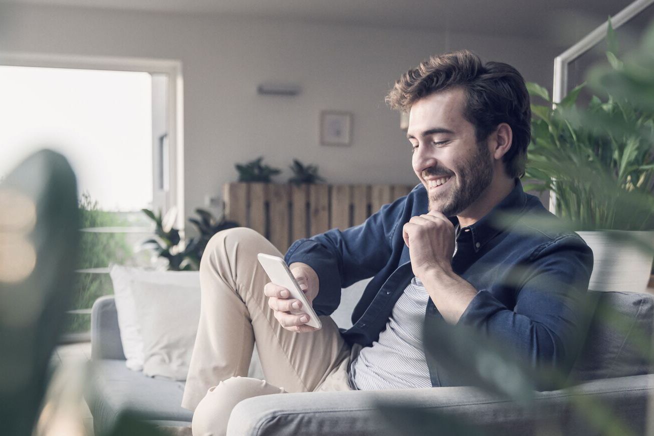 Nöjd man sitter i soffa och tittar på en dator