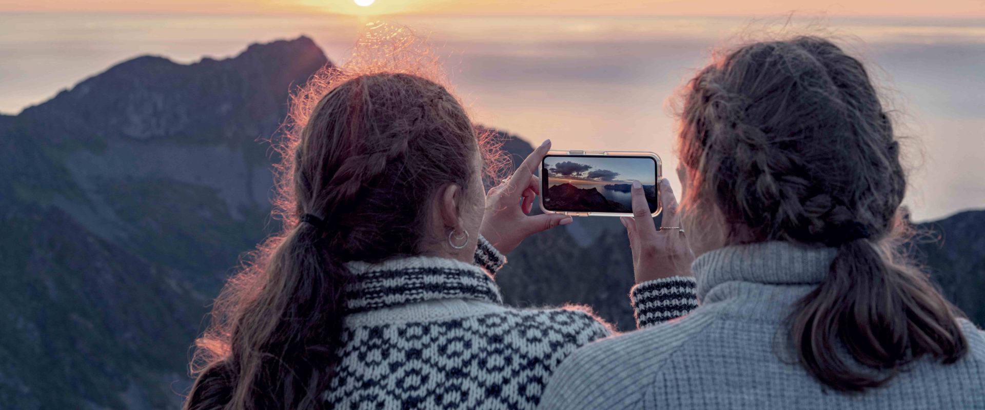 Women photographing sunset with smartphone
