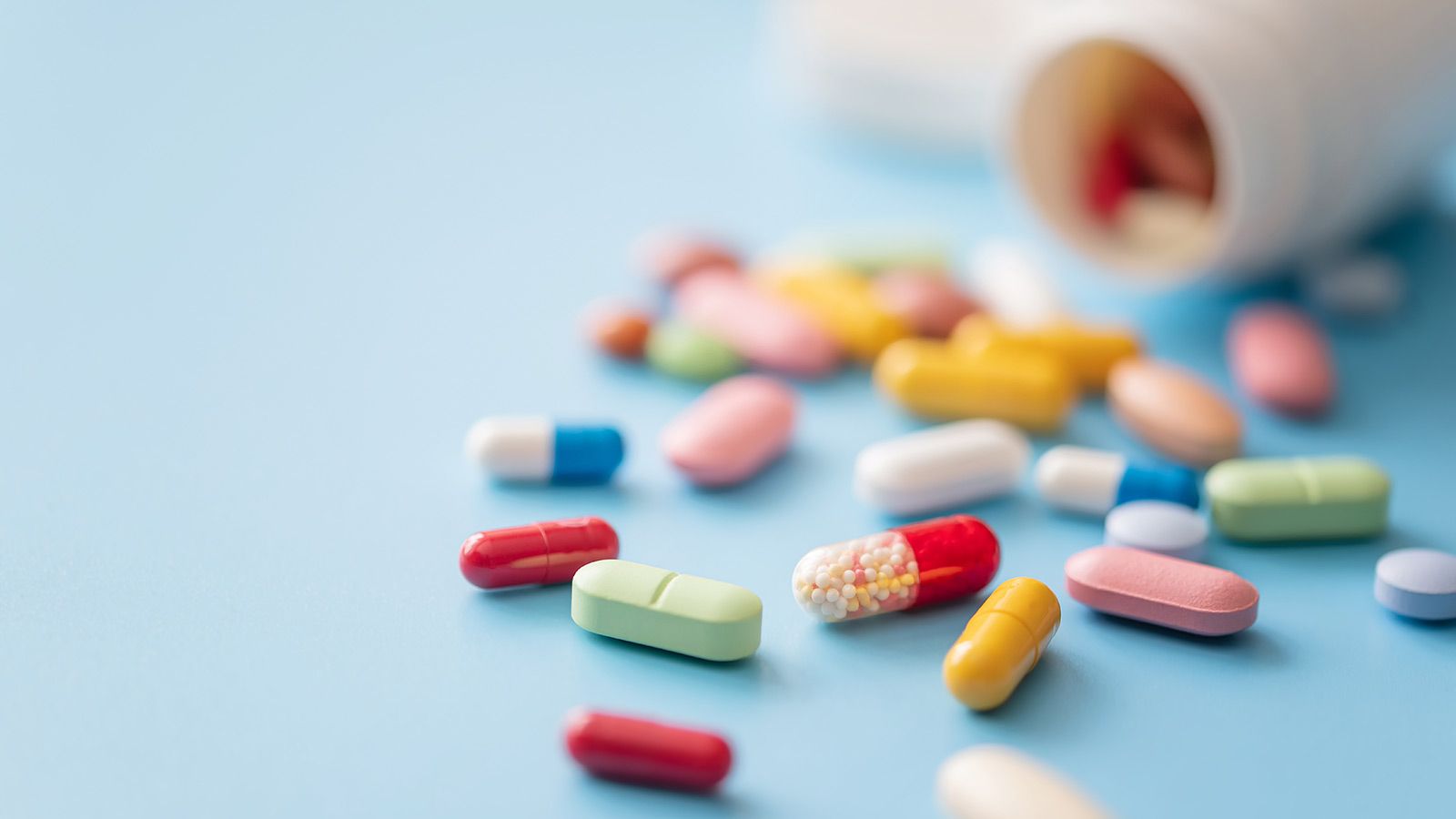 Multifarvede piller spredt fra hvid plastikmedicinbeholder