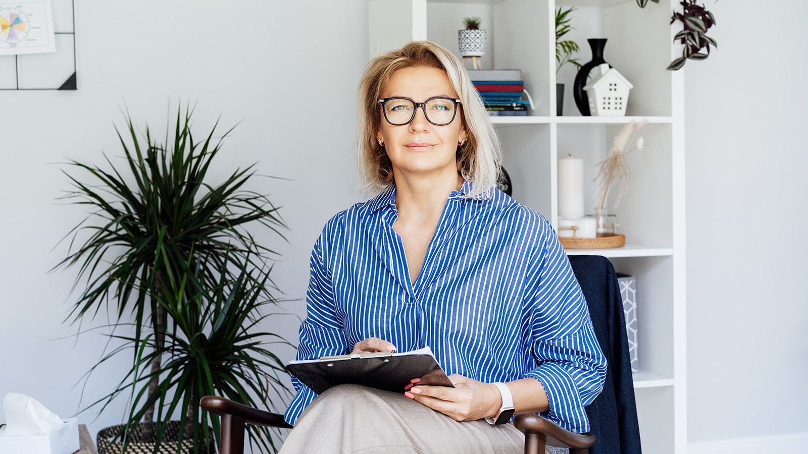 Professionel psykoterapi. Succesfuld kvindelig psykolog smilende til kamera sidder på lænestol på kontoret.