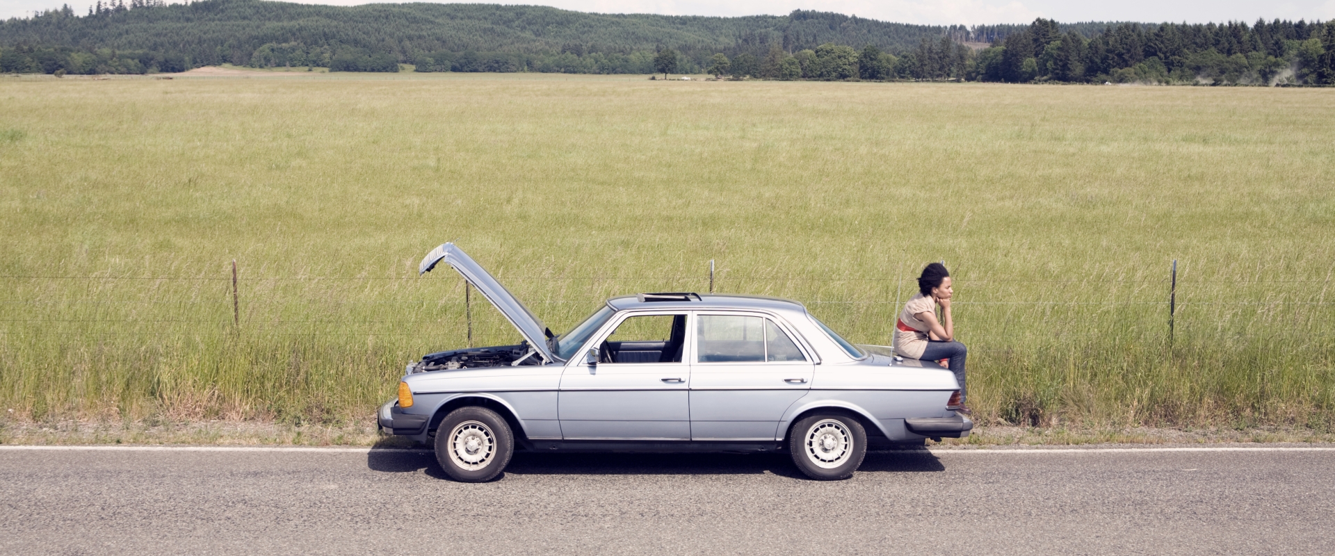 woman sitting on trunk of broken car.