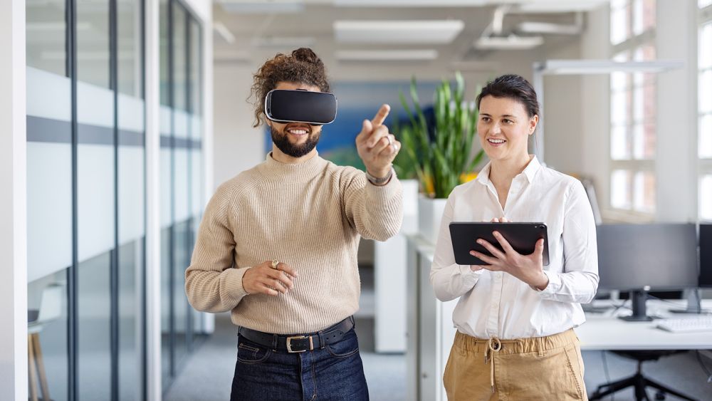 Glad forretningsmand bruger VR-briller af kollega, der arbejder på en digital tablet
