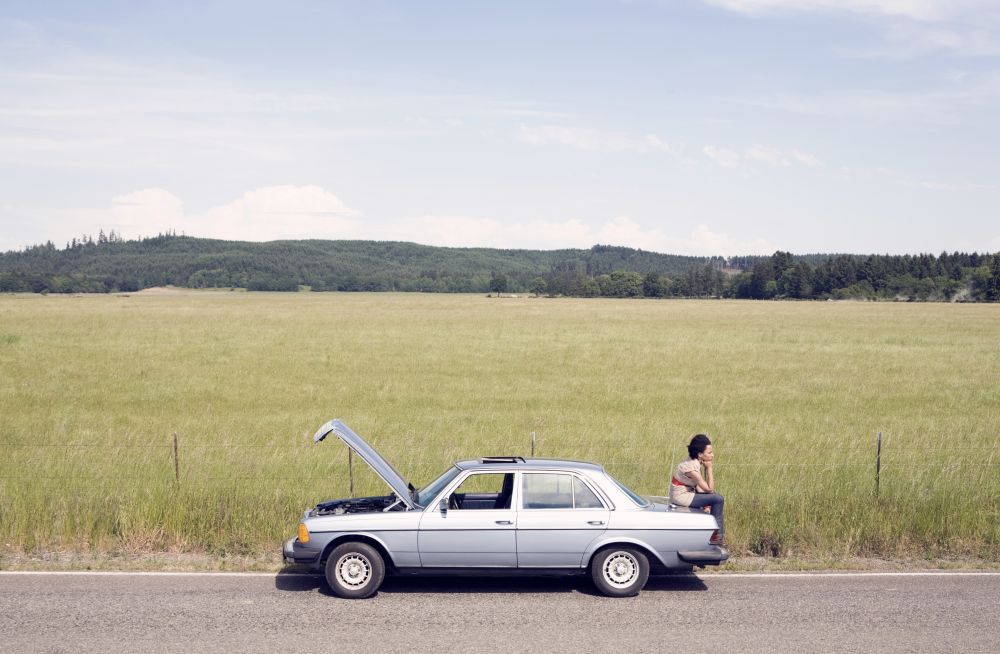 woman sitting on trunk of broken car.